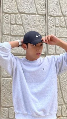 a young man is holding his hat over his head while standing in front of a brick wall