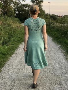 a woman in a green dress walking down a gravel road