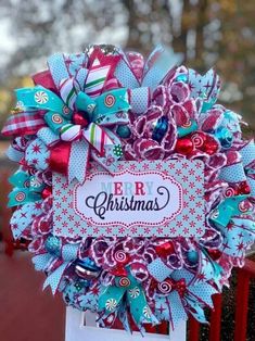 a colorful christmas wreath on top of a red fence with the word merry written in it