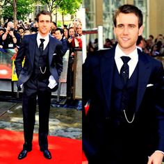 a man in a suit and tie standing on a red carpet next to a group of people