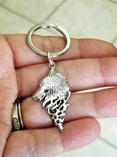 a hand holding a silver key chain with a wolf head on it's side