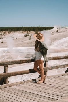 a woman standing on a wooden bridge in front of a geyser filled field