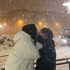 two people are standing in the snow with their arms around each other as they kiss