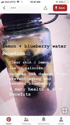 a person holding a water bottle filled with lemons and blueberry water on top of a table