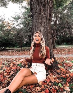 a woman sitting on the ground in front of a tree with leaves all around her