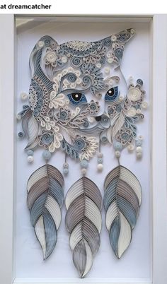 an art work made out of paper with blue eyes and feathers on the bottom, in a white frame