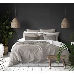 a bed with grey linens and pillows in a white room next to potted plants