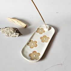 a white porcelain dish with flowers on it next to a wooden stick and some dried herbs