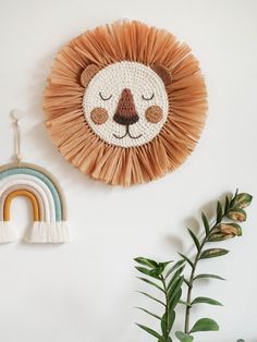 a wall hanging with a lion face on it and a rainbow in the middle, next to a potted plant