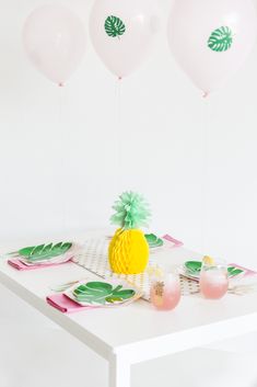 a pineapple on a table with pink and green plates, balloons and napkins