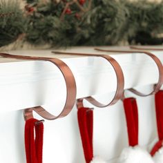 three christmas stockings hanging on a mantle with pine branches in the background and red ribbon