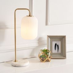 a white table topped with a lamp next to a framed photo and a small potted plant