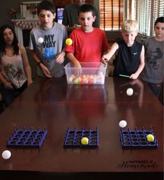 a group of young children standing around a table with balls in plastic containers on it