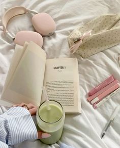 a person laying in bed reading a book and holding a cup with a drink next to it