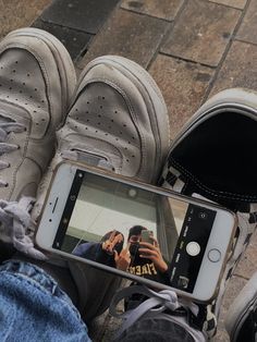 a person taking a photo with their cell phone while sitting on the ground next to two pairs of shoes