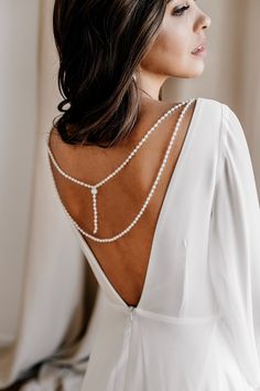 the back of a woman wearing a long white dress with pearls on it's neck