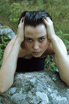 a woman leaning on a rock with her hands behind her head