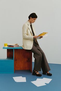 a woman sitting on top of a wooden table holding a book in her hand and reading