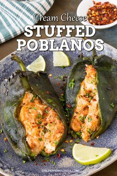 stuffed poblanos on a blue plate with lime wedges and chili in the background