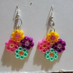 two pairs of colorful earrings hanging from hooks on a white surface with small circles attached to them