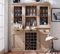 a wooden cabinet filled with lots of bottles and glasses next to a bar stool on top of a hard wood floor