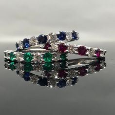 a multicolored diamond and emerald ring on top of a reflective surface with reflection