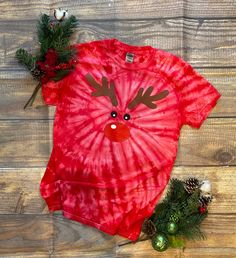 a red tie - dye shirt with a reindeer face on it and pine cones next to it