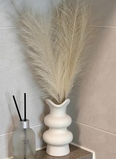 a white vase sitting on top of a counter next to a bottle with a feather in it