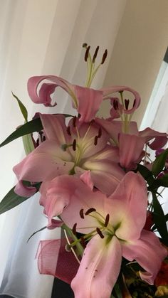 pink lilies in a vase on a table next to a window with sheer curtains