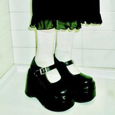 a woman's legs wearing black and white shoes in a bath room with tiled walls