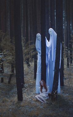 a woman is sitting in the middle of a forest with her arms wrapped around an object