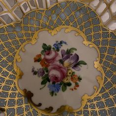 a plate with flowers painted on it sitting on top of a gold and blue table