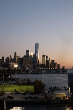 the city skyline is lit up at night as seen from across the water with cars parked in front of it