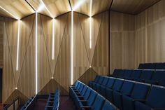 an empty auditorium with rows of blue seats and wooden walls, along with lights hanging from the ceiling