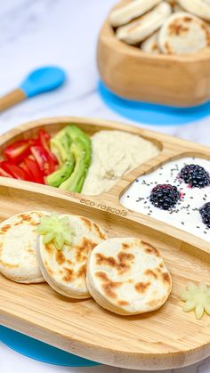 a wooden tray topped with food on top of a white table next to utensils