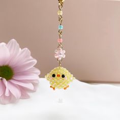 a yellow bird keychain hanging from a chain next to a pink flower on a table