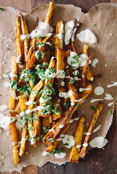 french fries covered in sour cream and parsley on a piece of parchment paper next to a wooden table