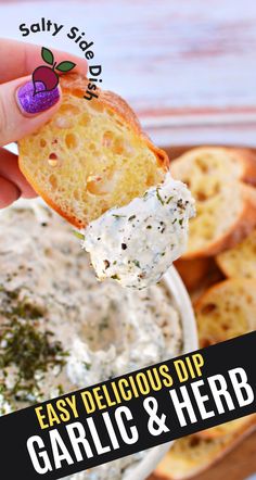 a hand holding a piece of bread with garlic and herb dip on it in front of some crackers