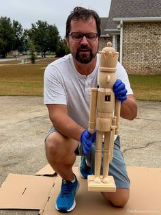 a man kneeling down next to a wooden toy figure holding a stick in his hand