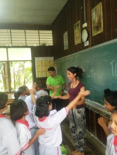 a group of children standing in front of a blackboard with an adult teaching them