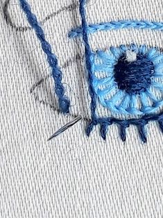 a close up of a piece of cloth with blue thread on it and an eye in the middle