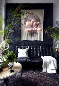 a living room with black leather couches and plants in front of a large poster