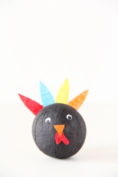 a paper mache bird with colored feathers on it's head and eyes, sitting on a white surface