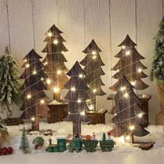 christmas trees with lights are displayed in front of a wooden wall and snow covered ground