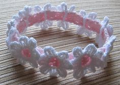 a crocheted bracelet with pink and white flowers on the end, sitting on a table