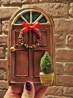 a hand holding up a cookie shaped like a door with a wreath and potted plant