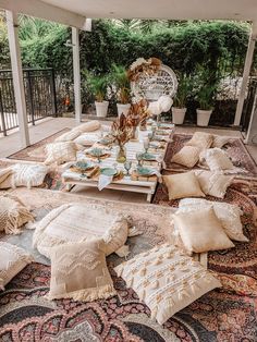 an outdoor dining area with lots of pillows and place settings on the rugs, along with potted plants