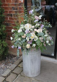 a bucket filled with lots of flowers sitting on top of a stone floor next to a brick wall