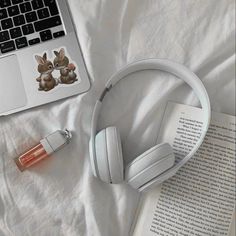 an open book and headphones on top of a bed next to a laptop computer