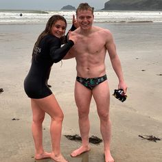 a man and woman standing on top of a sandy beach